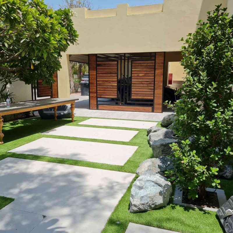 Beautifully landscaped garden with pathway and a pool surrounded by lush greenery in a Dubai residence, showcasing a well-maintained outdoor space.